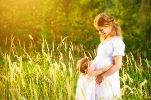 happy family, a pregnant mother and daughter little girl child in the summer meadow with yellow flowers